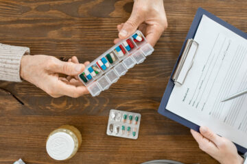 Overhead story of a patient and doctor reviewing health information on a clipboard, pill organizers and other health items