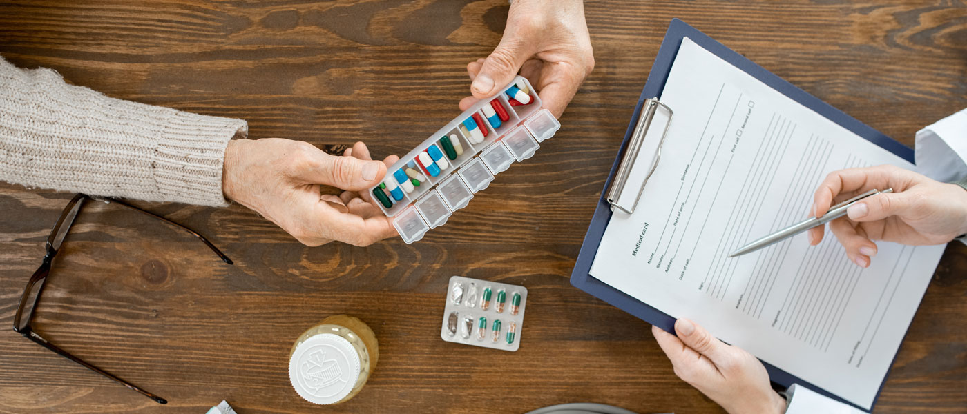 Overhead story of a patient and doctor reviewing health information on a clipboard, pill organizers and other health items