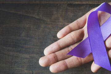 Photo of a hand holding a purple ribbon