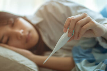 Photo of a woman laying in bed looking at a thermometer