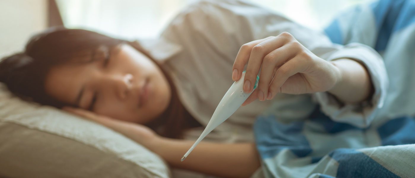 Photo of a woman laying in bed looking at a thermometer