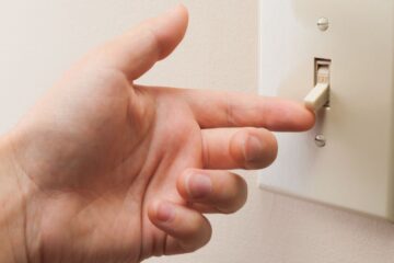 Hand turning wall light switch off, courtesy of Getty Images.