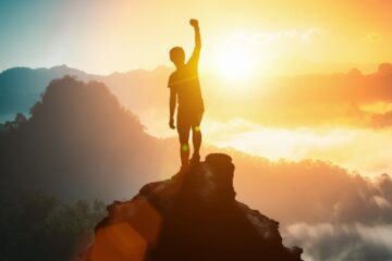 Silhouette of positive man celebrating on mountain top, with arms raised up. Business, success,victory,leadership,achievement concept. Courtesy of Getty Images.