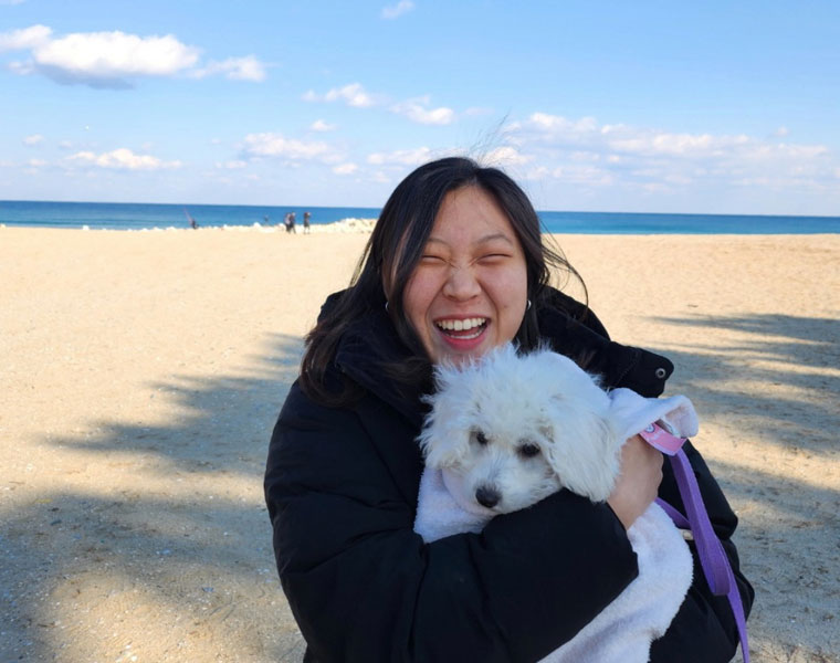 Photo of Erum Jang hugging a dog on a beach