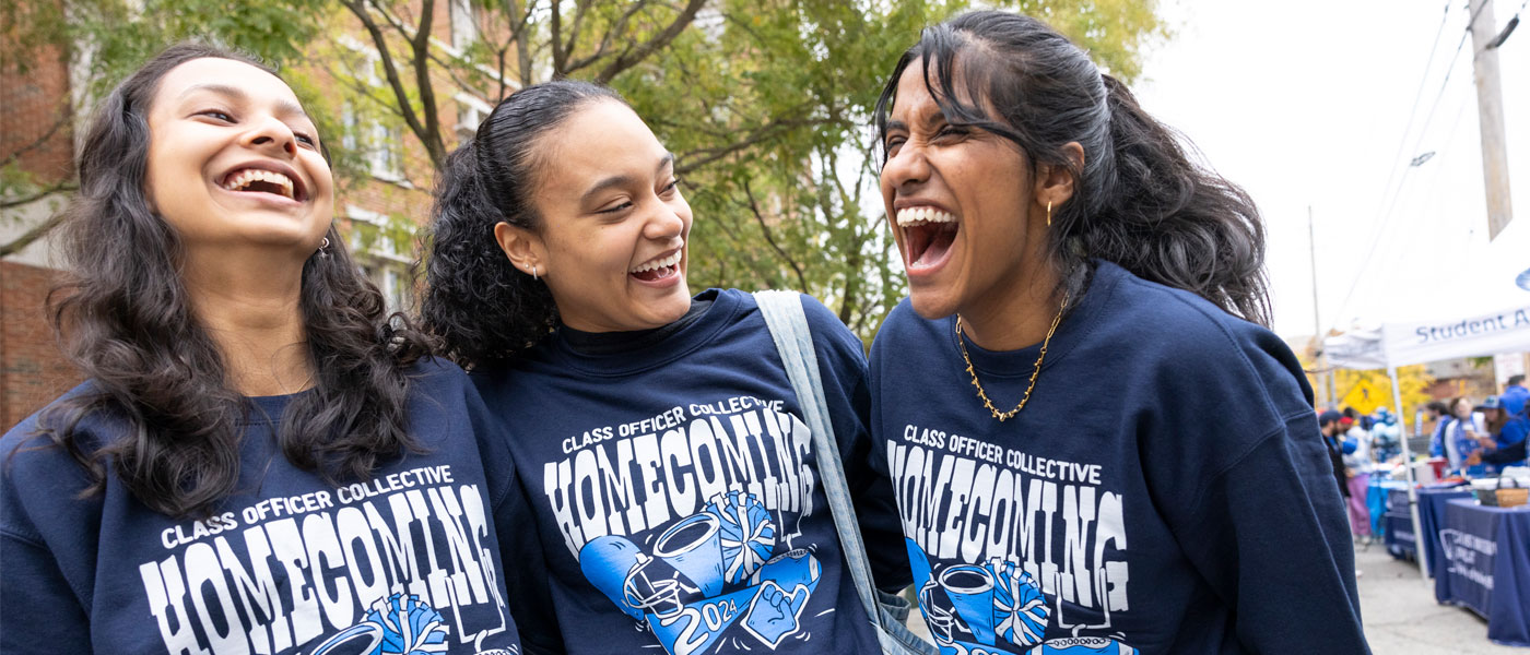 Photo of three smiling and laughing students posing for a photo during homecoming festivities