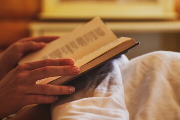 Close up of woman reading a book in bed, courtesy of Getty Images.