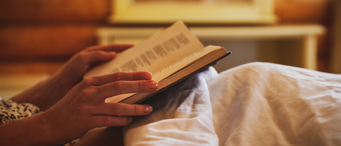 Close up of woman reading a book in bed, courtesy of Getty Images.