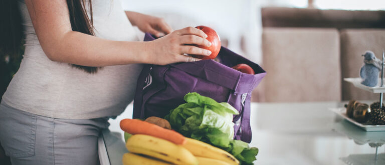 Close up photo of a pregnant woman taking produce out of a bag