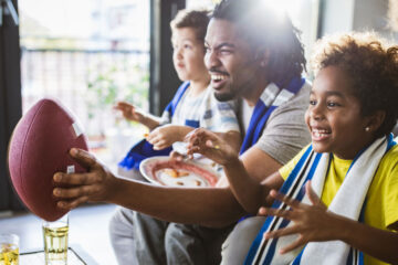 Photo of a young family watching a football game at home and cheering